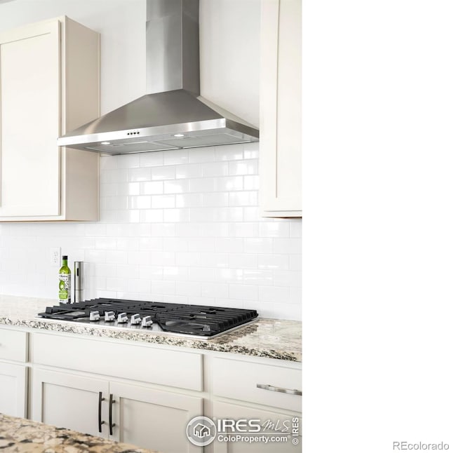 kitchen featuring wall chimney exhaust hood, stainless steel gas cooktop, backsplash, and white cabinetry