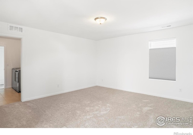 unfurnished room featuring separate washer and dryer, light colored carpet, and baseboards