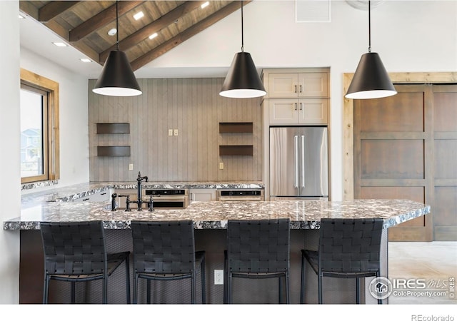 kitchen with stainless steel appliances, a sink, light stone counters, a breakfast bar area, and hanging light fixtures