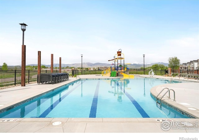 community pool featuring fence, a mountain view, and a water slide