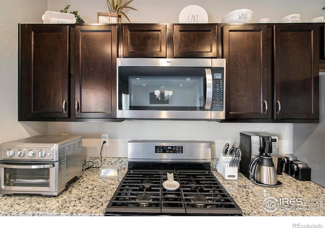 kitchen with stainless steel appliances, dark brown cabinets, and light stone countertops