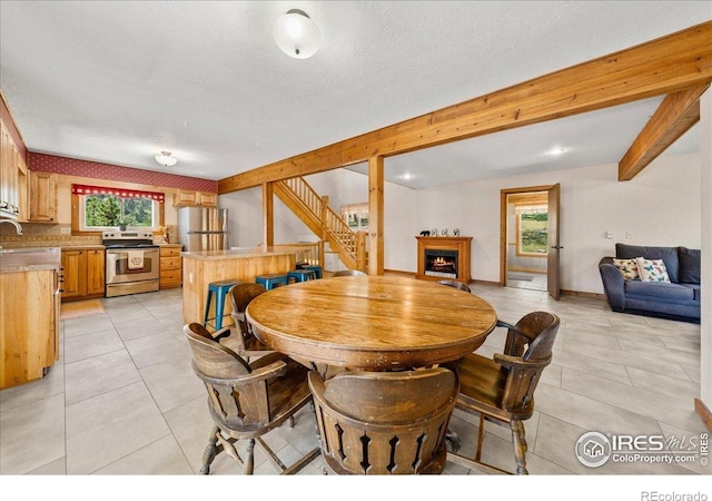 457 Spruce Mountain Dr, Drake, CO 80515 - dining space with stairway, a warm lit fireplace, beamed ceiling, and light tile patterned flooring