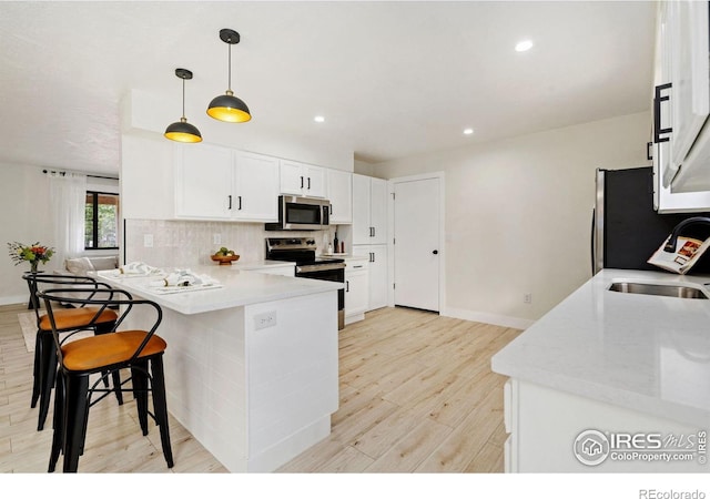kitchen with appliances with stainless steel finishes, a sink, light wood finished floors, a peninsula, and a breakfast bar
