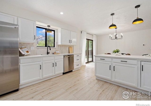 kitchen featuring appliances with stainless steel finishes, a sink, a chandelier, tasteful backsplash, and light wood finished floors