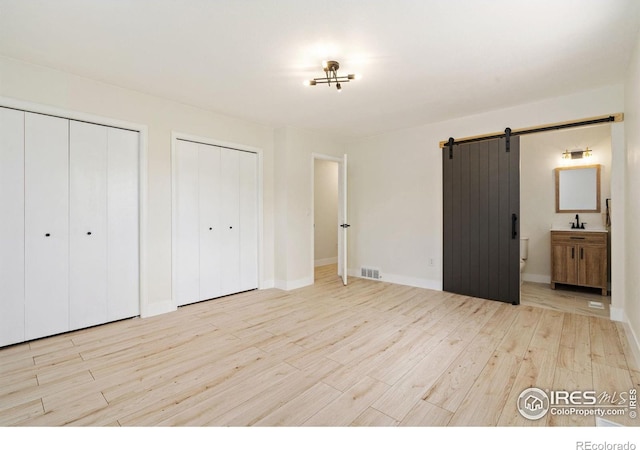 unfurnished bedroom featuring multiple closets, a barn door, wood finished floors, a sink, and ensuite bathroom