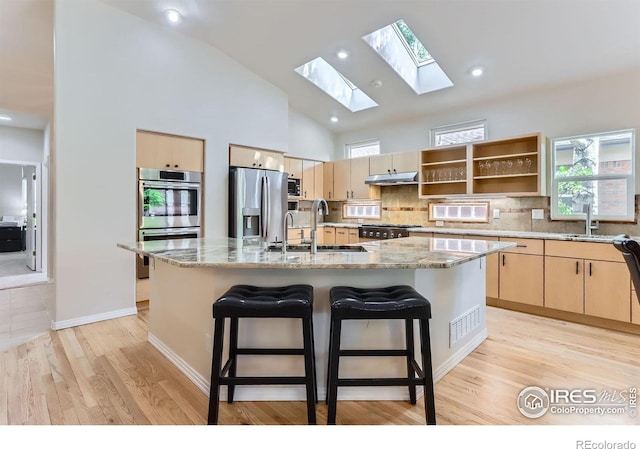 kitchen with stainless steel appliances, a sink, a skylight, light brown cabinets, and light stone countertops