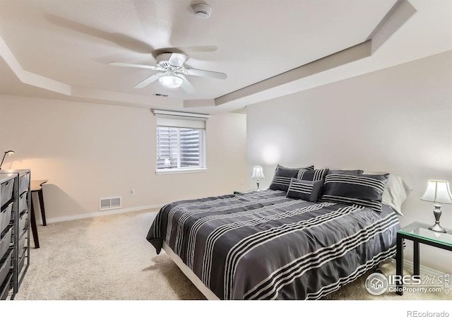 carpeted bedroom with a raised ceiling, baseboards, and ceiling fan