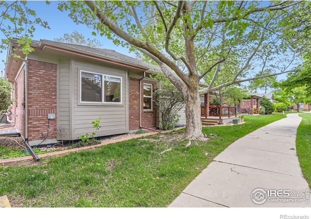 view of front of property featuring brick siding, a front lawn, and a wooden deck
