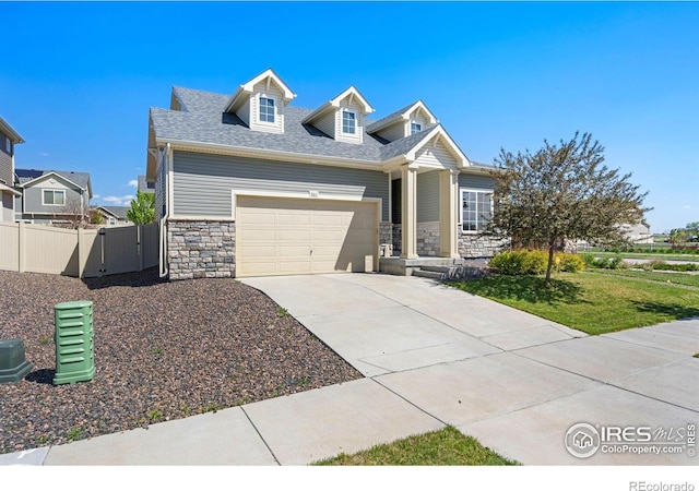 view of front of property with stone siding, concrete driveway, a garage, fence, and a shingled roof
