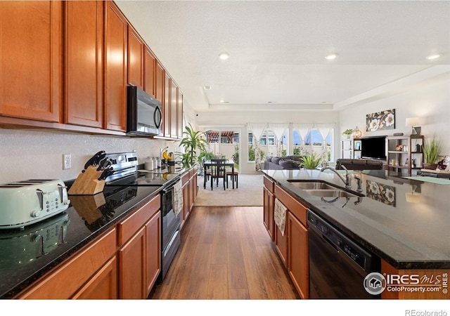 kitchen with black appliances, a sink, open floor plan, dark wood-style flooring, and an island with sink