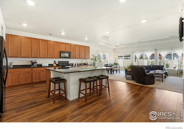 kitchen with black appliances, plenty of natural light, dark wood-type flooring, recessed lighting, and a kitchen bar