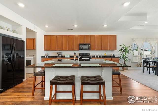 kitchen with washer / dryer, black appliances, dark countertops, a breakfast bar area, and recessed lighting