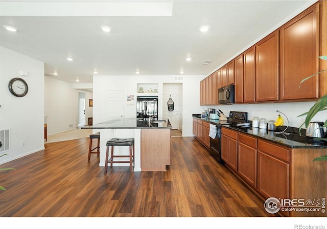 kitchen featuring black appliances, dark wood finished floors, a kitchen bar, an island with sink, and recessed lighting