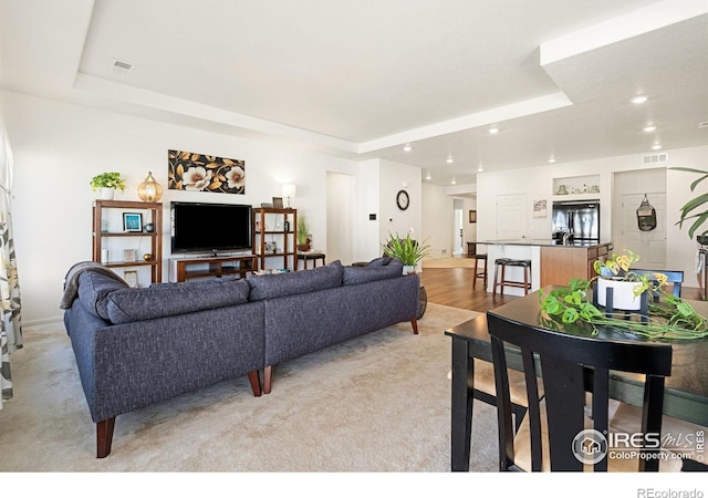 living area with a tray ceiling, recessed lighting, and light carpet