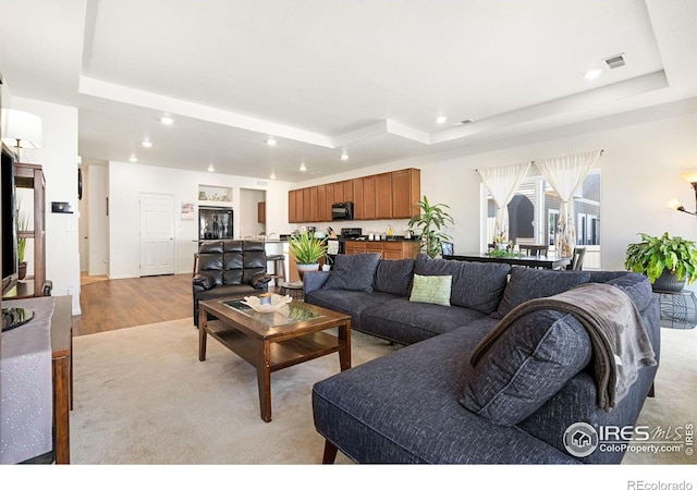 living room featuring a tray ceiling, recessed lighting, and light wood finished floors