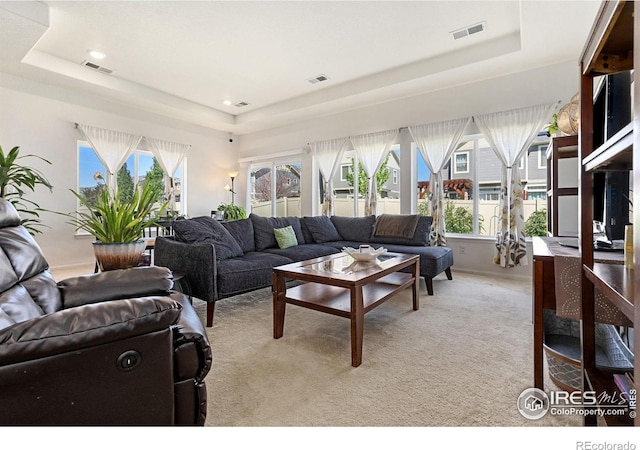 living room featuring a raised ceiling, healthy amount of natural light, light carpet, and recessed lighting