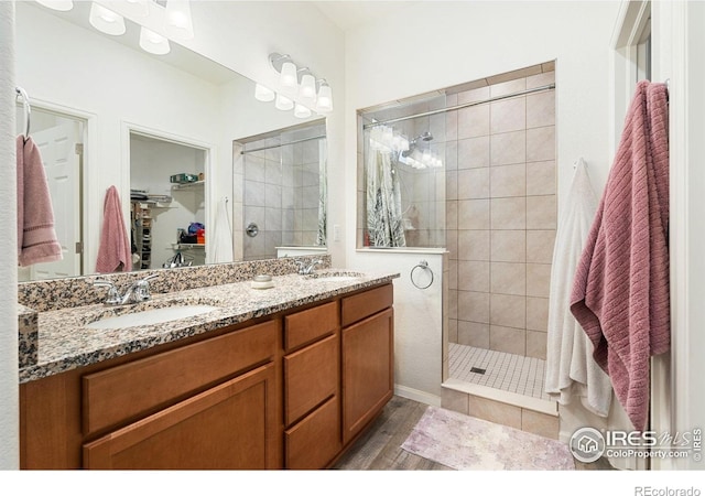 full bath featuring tiled shower, wood finished floors, double vanity, and a spacious closet