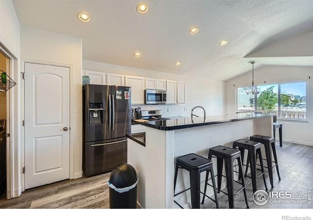 4134 Cypress Ridge Ln, Wellington, CO 80549 - kitchen featuring stainless steel appliances, wood finished floors, white cabinetry, a kitchen breakfast bar, and lofted ceiling