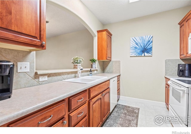 kitchen with a sink, white appliances, tasteful backsplash, and light countertops