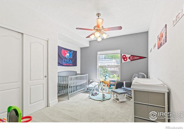 carpeted bedroom with a crib, a closet, and ceiling fan