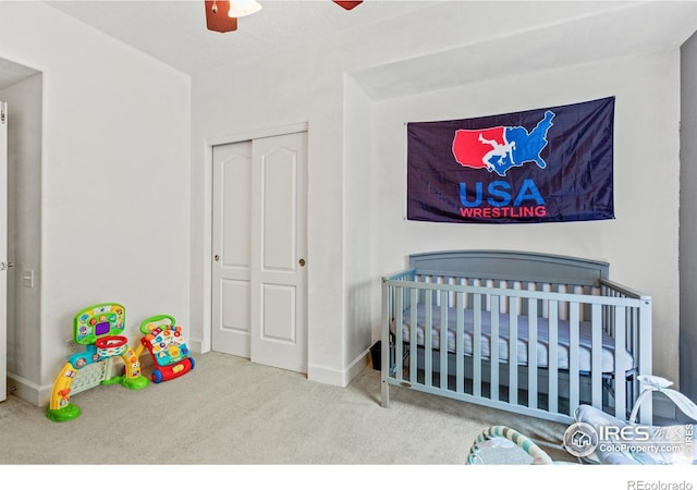 carpeted bedroom with a closet, a crib, ceiling fan, and baseboards