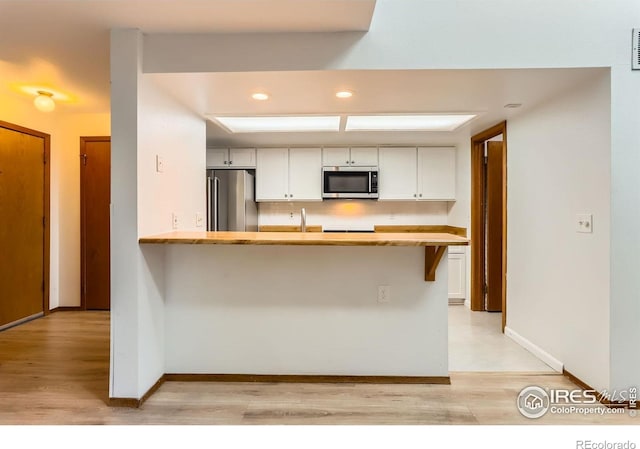 2962 Shadow Creek Dr Unit 306, Boulder, CO 80303 - kitchen with appliances with stainless steel finishes, light wood-style flooring, white cabinetry, a peninsula, and light countertops