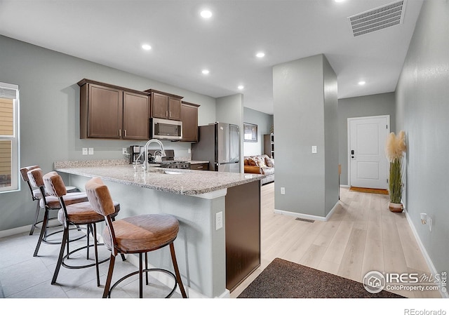 kitchen with stainless steel appliances, a kitchen breakfast bar, baseboards, a sink, and a peninsula