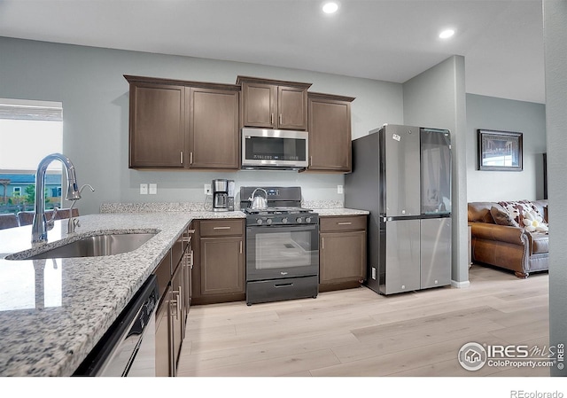 kitchen with stainless steel appliances, a sink, light stone counters, light wood-type flooring, and dark brown cabinets