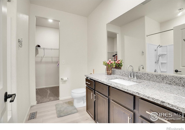 full bath featuring wood finished floors, toilet, vanity, a walk in closet, and baseboards