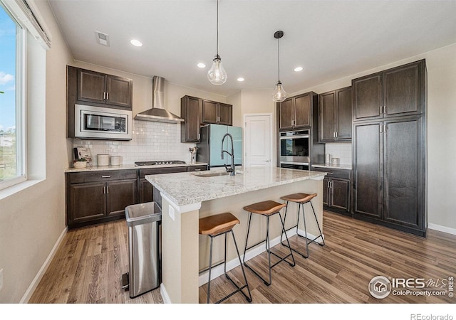 6009 Autumn Breeze Ct, Fort Collins, CO 80528 - kitchen featuring wall chimney range hood, stainless steel appliances, dark brown cabinets, decorative backsplash, and recessed lighting