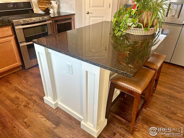 8241 White Owl Ct, Windsor, CO 80550 - kitchen featuring range with two ovens, dark stone countertops, a breakfast bar area, and dark wood-style floors