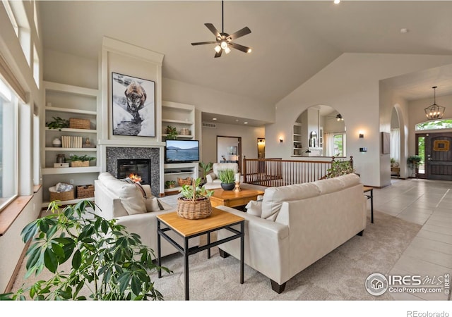 7717 Amour Hill Dr, Greeley, CO 80634 - living room featuring arched walkways, a glass covered fireplace, light tile patterned flooring, a ceiling fan, and high vaulted ceiling