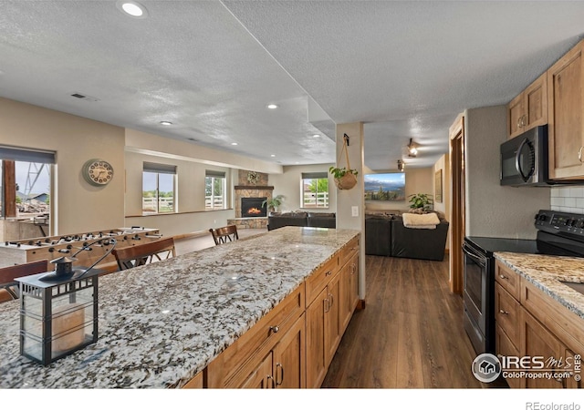 7717 Amour Hill Dr, Greeley, CO 80634 - kitchen featuring black electric range, open floor plan, dark wood finished floors, a stone fireplace, and a textured ceiling