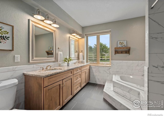 7717 Amour Hill Dr, Greeley, CO 80634 - bathroom featuring tile walls, double vanity, toilet, a bath, and wainscoting