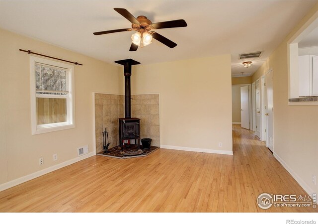 503 E Oak St, Lafayette, CO 80026 - unfurnished living room featuring a wood stove, light wood-style floors, a ceiling fan, and baseboards