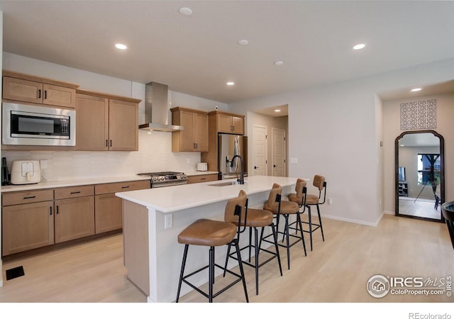 5282 Ribault St, Timnath, CO 80547 - kitchen featuring wall chimney range hood, stainless steel appliances, light wood-type flooring, an island with sink, and recessed lighting