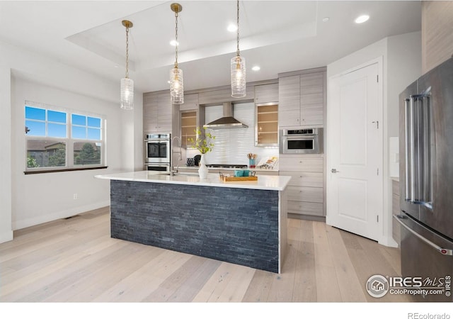4014 Rock Creek Dr, Fort Collins, CO 80528 - kitchen featuring appliances with stainless steel finishes, a tray ceiling, wall chimney exhaust hood, light wood-style flooring, and recessed lighting