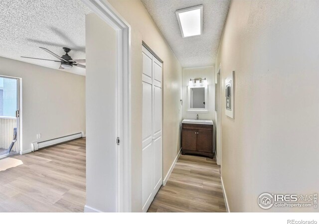 4110 Hale Pkwy # 5F, Denver, CO 80220 - hallway featuring a textured ceiling, a baseboard radiator, light wood finished floors, a sink, and baseboards
