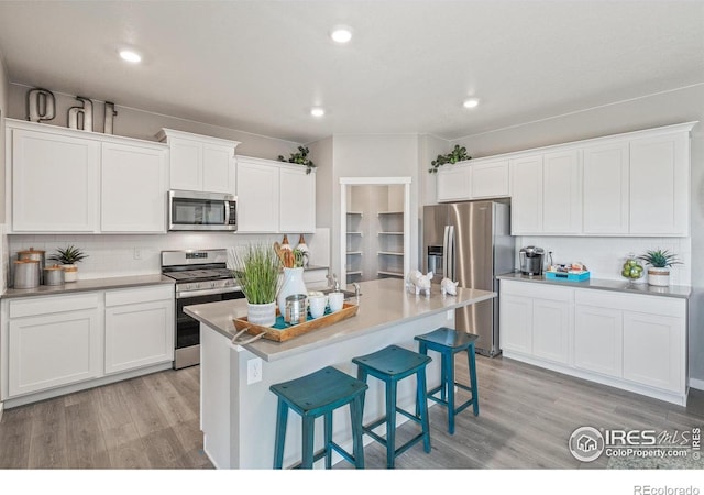 kitchen featuring stainless steel appliances, light wood-style floors, a breakfast bar area, decorative backsplash, and white cabinetry
