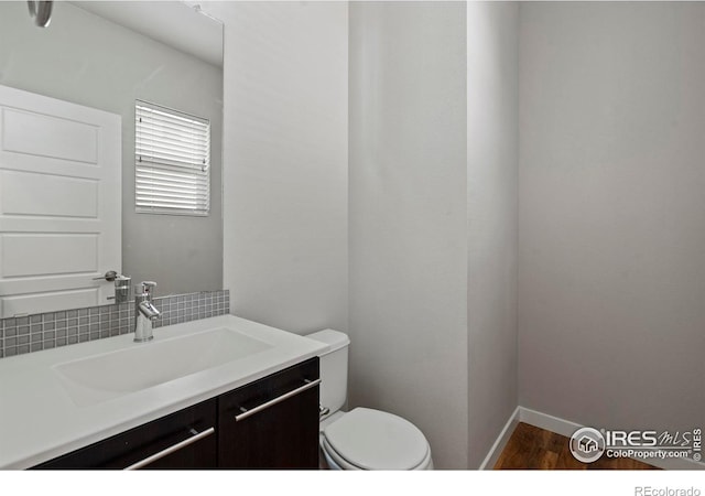 10069 Richfield St, Commerce City, CO 80022 - bathroom with wood finished floors, toilet, vanity, baseboards, and decorative backsplash