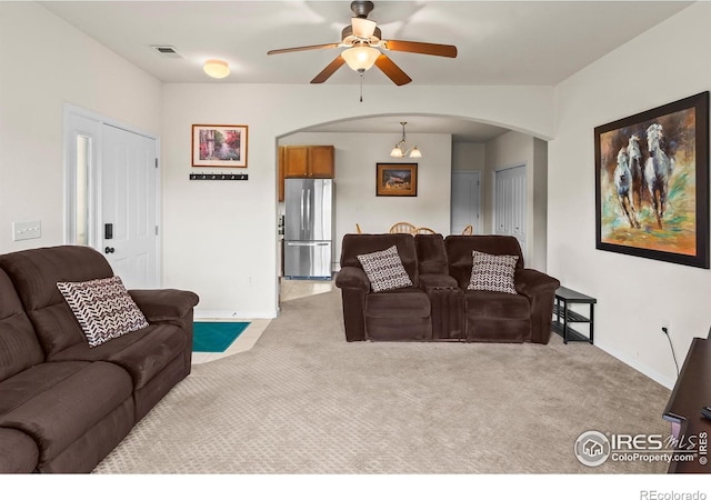 living area featuring arched walkways, light carpet, a ceiling fan, and baseboards