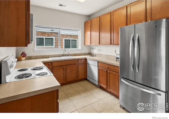 kitchen with white appliances, a sink, light tile patterned flooring, light countertops, and brown cabinetry