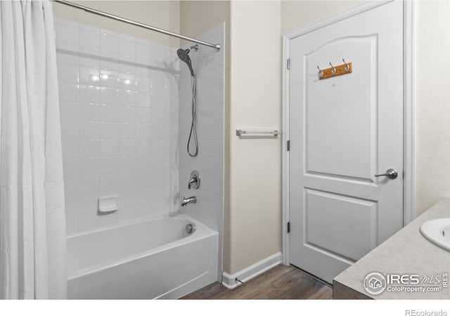 bathroom featuring wood finished floors, baseboards, shower / bath combo with shower curtain, and a sink
