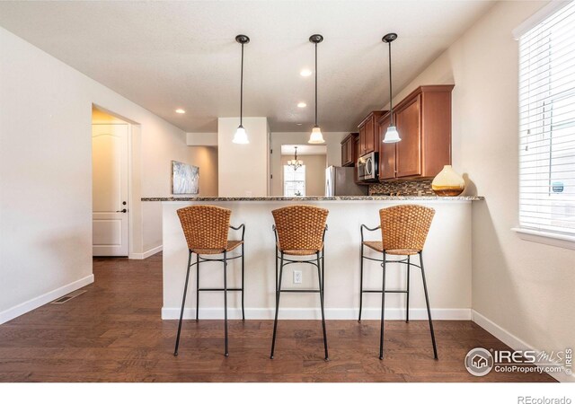1358 14th Ave, Longmont, CO 80501 - kitchen with stainless steel appliances, brown cabinetry, a kitchen breakfast bar, dark stone countertops, and dark wood-style flooring