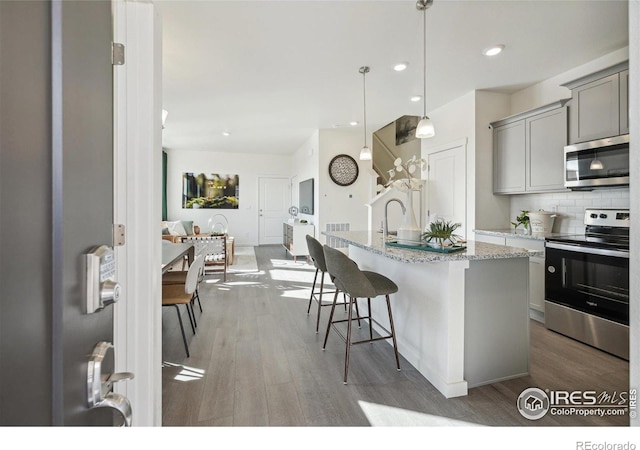 18722 E 99th Ave, Commerce City, CO 80022 - kitchen featuring appliances with stainless steel finishes, gray cabinetry, wood finished floors, backsplash, and a breakfast bar