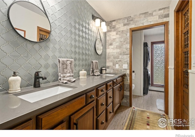 4456 W Pioneer Dr, Greeley, CO 80634 - bathroom featuring wood finished floors, double vanity, a baseboard radiator, stacked washer / drying machine, and toilet