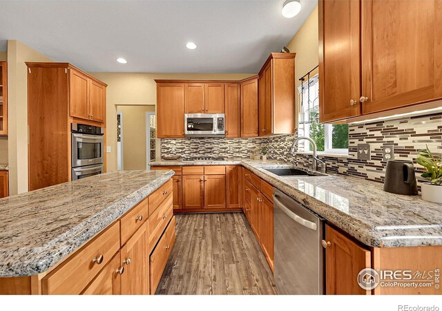 4764 Maggie Ct, Loveland, CO 80537 - kitchen with appliances with stainless steel finishes, a sink, light wood finished floors, decorative backsplash, and brown cabinets
