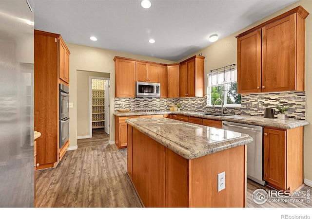 4764 Maggie Ct, Loveland, CO 80537 - kitchen featuring appliances with stainless steel finishes, a sink, light wood-type flooring, a center island, and tasteful backsplash