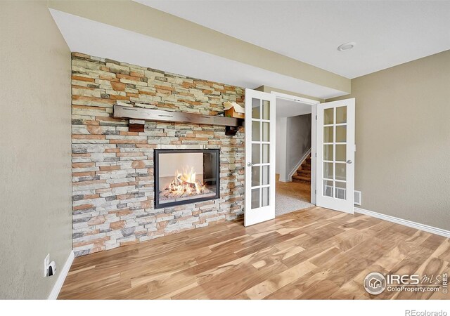4764 Maggie Ct, Loveland, CO 80537 - unfurnished living room featuring french doors, wood finished floors, baseboards, and a stone fireplace