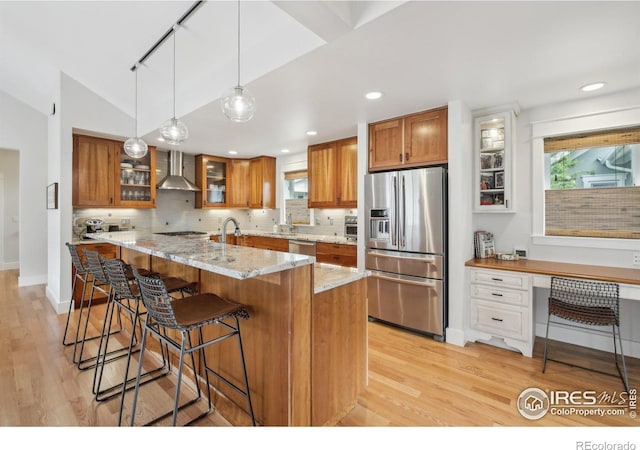 2917 13th St, Boulder, CO 80304 - kitchen featuring appliances with stainless steel finishes, wall chimney exhaust hood, brown cabinetry, light wood-type flooring, and decorative backsplash